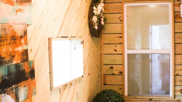 L’intérieur d’une cabane en bois, avec une fenêtre, un meuble blanc et un vase.