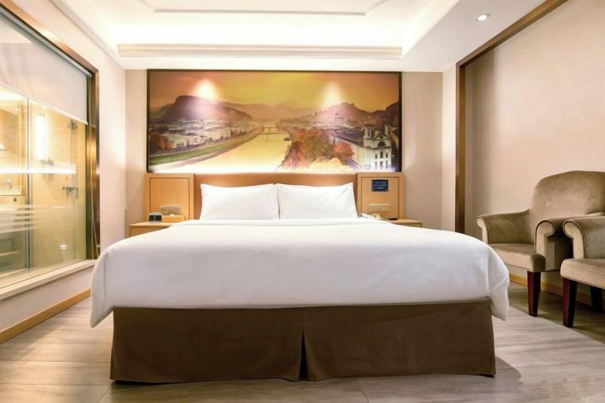 A hotel room with a large bed, a nightstand, a chair, and a wall mural.