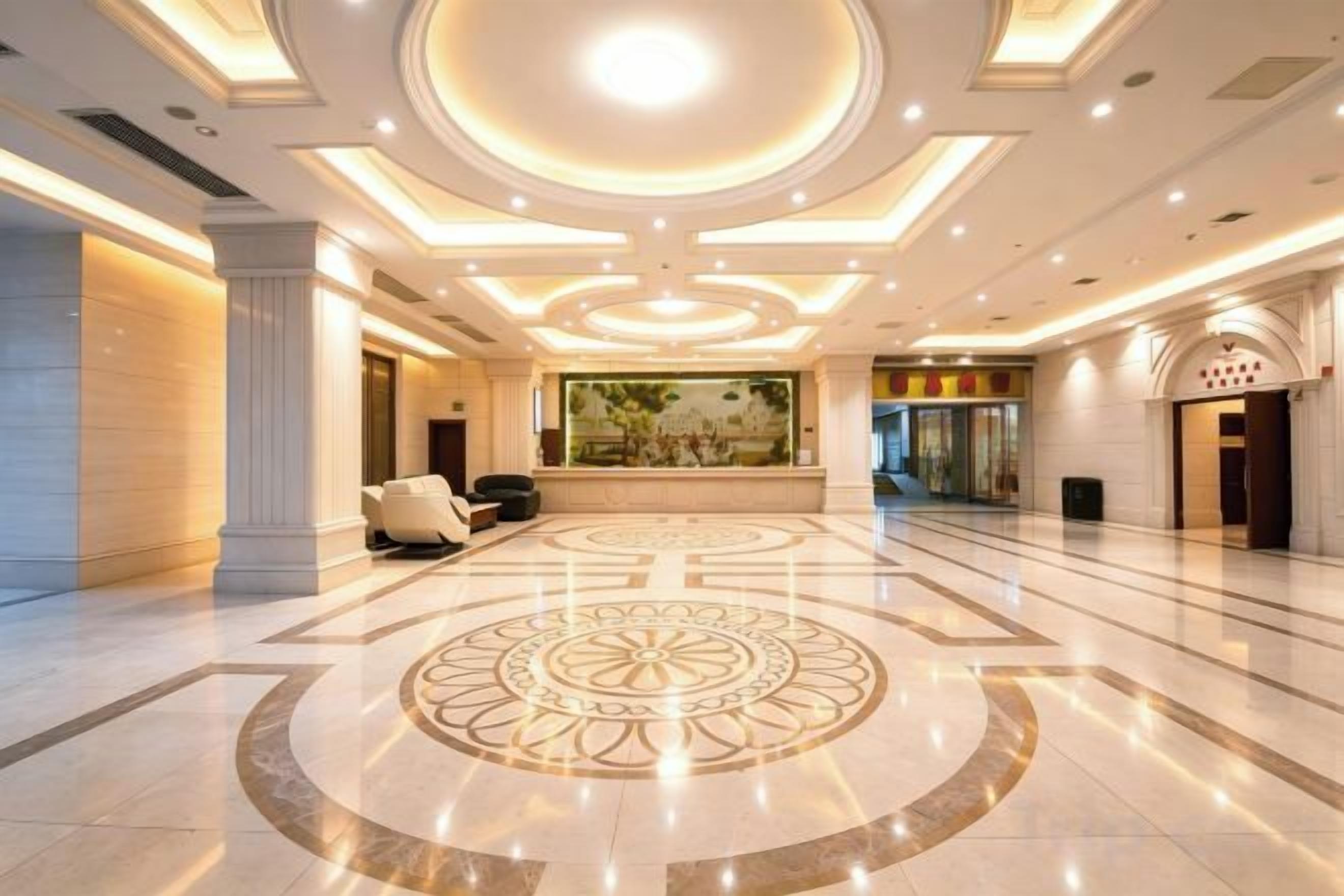 A spacious lobby with a central circular floor design, a reception desk, and a large mural on the wall.
