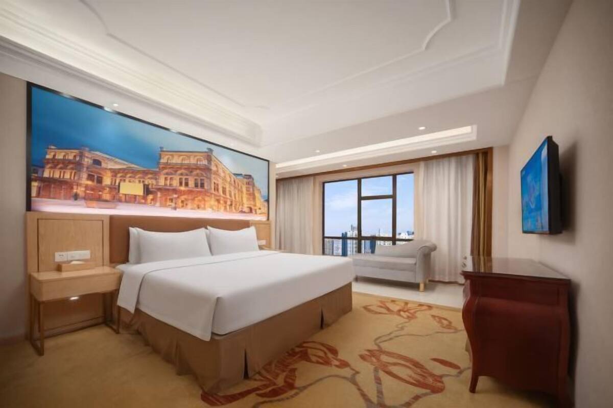 A hotel room with a large bed, a desk, a television, and a window with curtains.