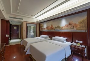 Una habitació d'hotel amb dos llits, un amb fusta al capçal, un quadre d'edifici, un escriptori amb un telèfon i una porta que dona a una altra habitació.