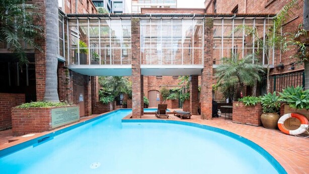 Una piscina con techo de vidrio, rodeada de muros de ladrillo y plantas en macetas.