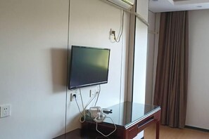 Habitación de hotel con una televisión de pantalla plana montada en la pared, una mesita de noche de madera y una ventana con cortinas.
