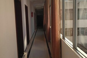 A hallway with doors on the left, a fire extinguisher on the wall, and a window on the right.
