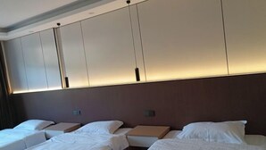 Une chambre d’hôtel avec quatre lits disposés en rangée, une grande armoire et un design moderne.