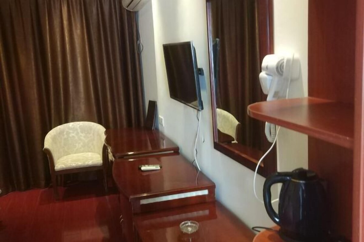 A hotel room with a wooden desk, a chair, a flat-screen TV, a mirror, a hairdryer, and a coffee maker.