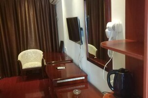 Habitación de hotel con un escritorio de madera, una silla, un televisor de pantalla plana, un espejo, un secador de pelo y una cafetera.