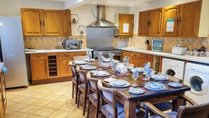 A kitchen with wooden cabinets, a stainless steel range hood, a built-in oven, a washing machine, and a dining table set for six with blue and white plates. - 3 bedroom accommodation in Onecote (Onecote)