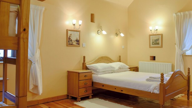 A bedroom with a wooden bed, bedside tables, a radiator, and wall-mounted lights. - 3 bedroom accommodation in Onecote (Onecote)