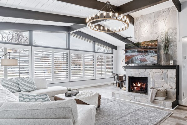 A modern living room with a stone fireplace, large windows, and a comfortable seating area.