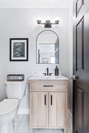 A modern bathroom with a white toilet, a wooden vanity with a mirror, and a light fixture above the sink.