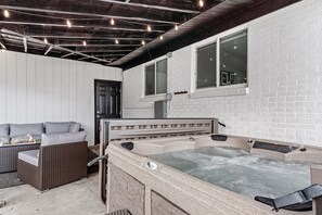 A spa area with a hot tub, wicker furniture, and a brick wall.