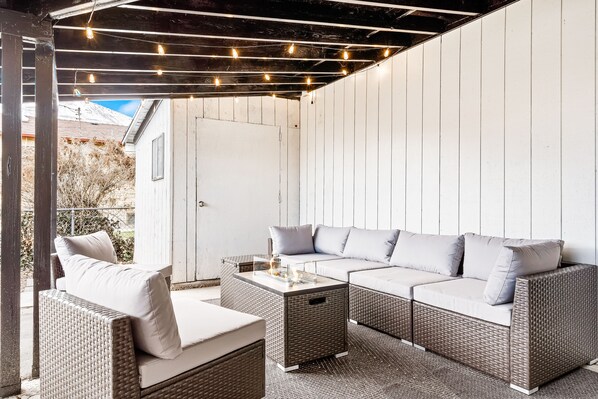 Eine Terrassengruppe im Freien mit Korbmöbeln, darunter eine Couch und Stühle, unter einer Pergola mit Lichterketten.