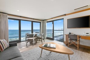 A modern hotel room with a large window overlooking the sea, a flat-screen TV, a desk, and a comfortable seating area. - SA Beach Suites (Malibu)