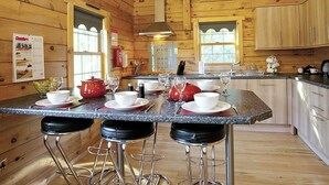 A wooden cabin kitchen with a central island, bar stools, and a dining table set for four.
