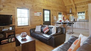 A cozy cabin interior with a leather sofa, a TV, and a wooden dining area.