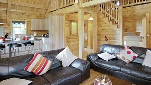 A spacious cabin interior with a dining area, kitchen, and two leather sofas with cushions.