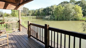 A wooden deck with a railing overlooking a calm river, surrounded by lush greenery.