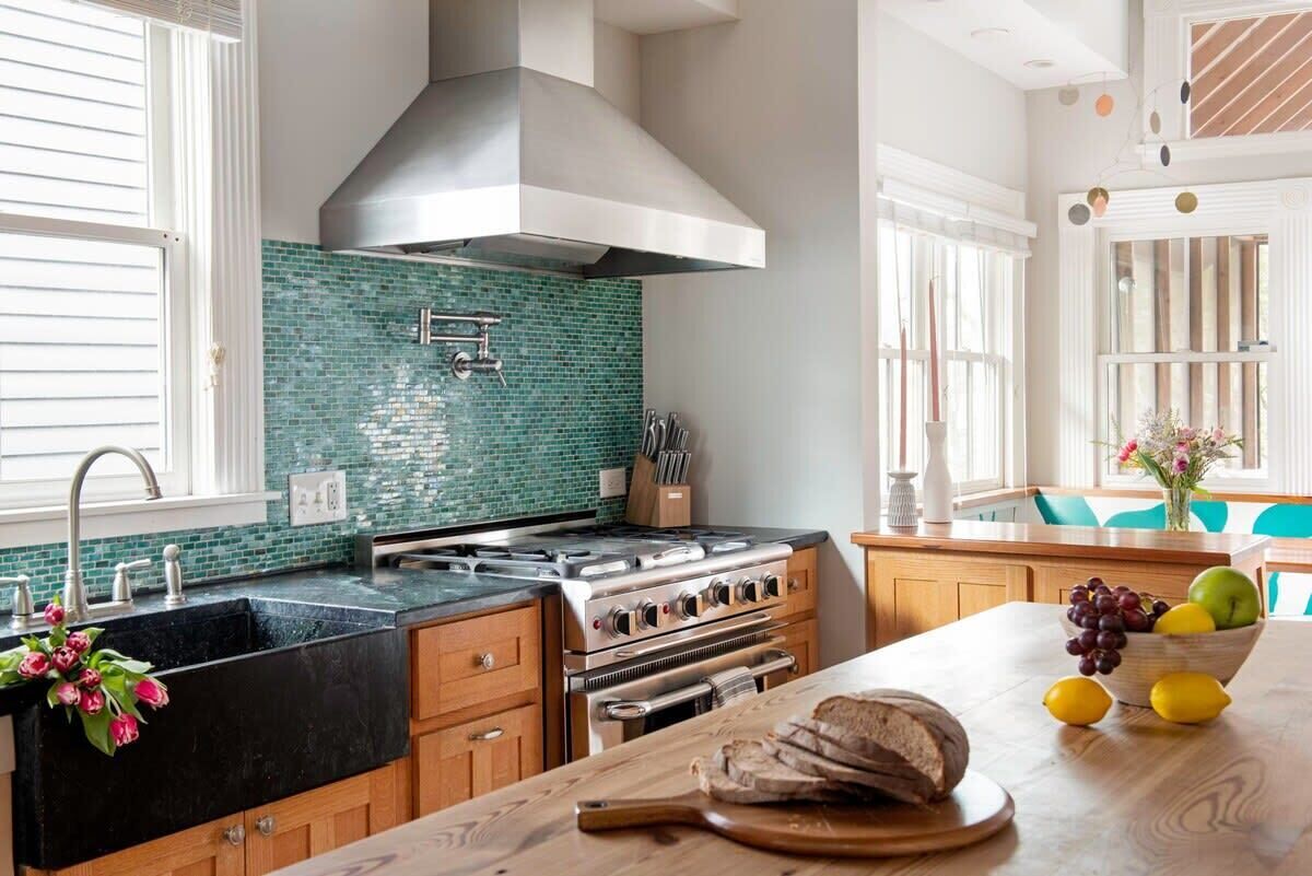 Een moderne keuken met een zwart aanrecht, een roestvrijstalen fornuis en een groene betegelde achterwand.