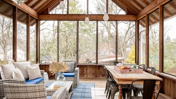 Una habitación amplia con ventanas grandes, techo de madera, mobiliario de mimbre y una mesa de comedor.