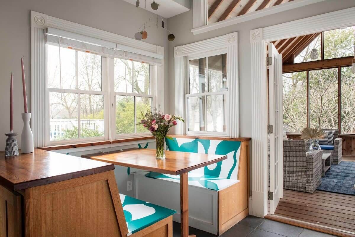 Una cocina con una mesa y banco de madera, ventanas amplias y vistas al exterior.
