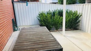 Un espace patio avec un banc en bois, une clôture blanche et des arbustes verts.