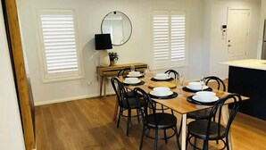 Un coin repas avec une table en bois et des chaises noires, de l’assiette blanche et un miroir au mur.