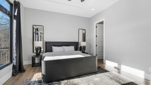 A modern bedroom with a large bed, two bedside tables with lamps, and a large window with curtains. - Modern Luxury! Sleeps 24! Pool, Spa, Golf, Arcade, Dock! Deep Cove, Calm Waters! (Sunrise Beach)