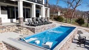A rectangular swimming pool with a stone border, surrounded by a patio with lounge chairs and a stone wall. - Modern Luxury! Sleeps 24! Pool, Spa, Golf, Arcade, Dock! Deep Cove, Calm Waters! (Sunrise Beach)