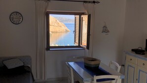 Una stanza con un tavolo da pranzo, sedie, un divano, una finestra vista mare e un orologio appeso al muro.