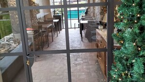 Une porte vitrée donne accès à une salle à manger avec un espace extérieur aménagé, une guirlande décorative et un sapin de Noël.