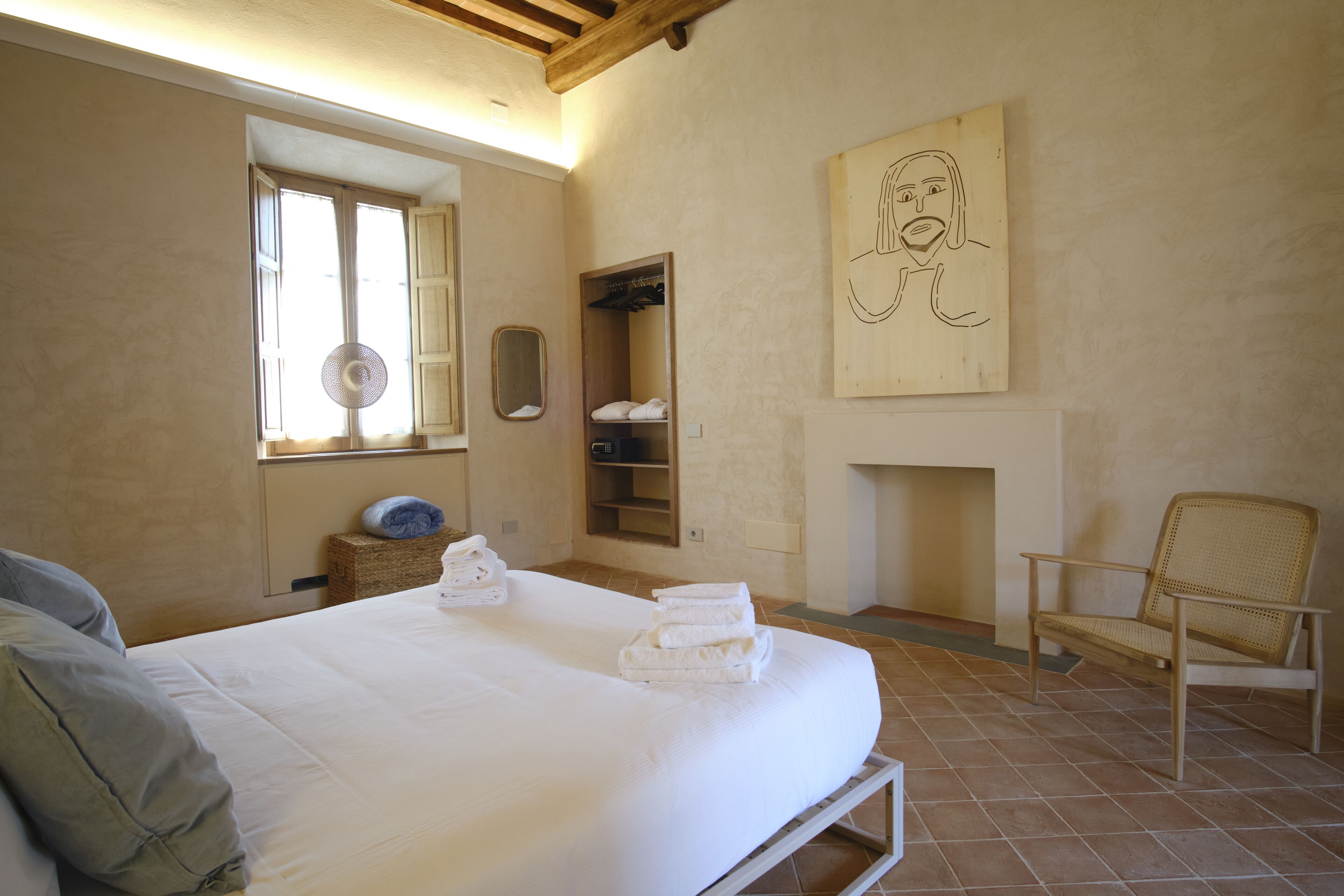A bedroom with a bed, a wooden chair, a fan, a fireplace, and a wooden artwork on the wall.