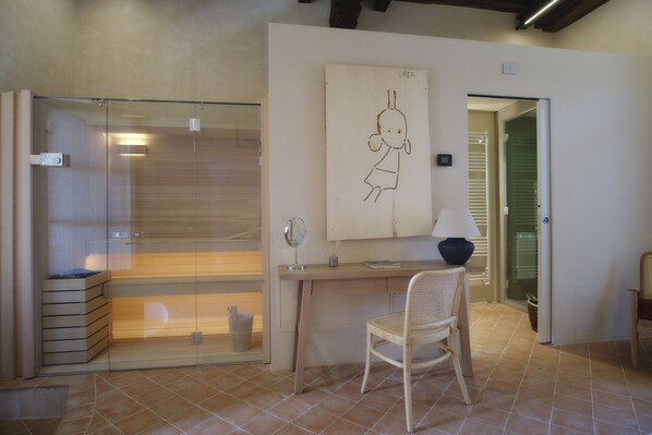 Un baño moderno con cabina de ducha de vidrio, un escritorio de madera, una silla y una obra de arte colgada en la pared.