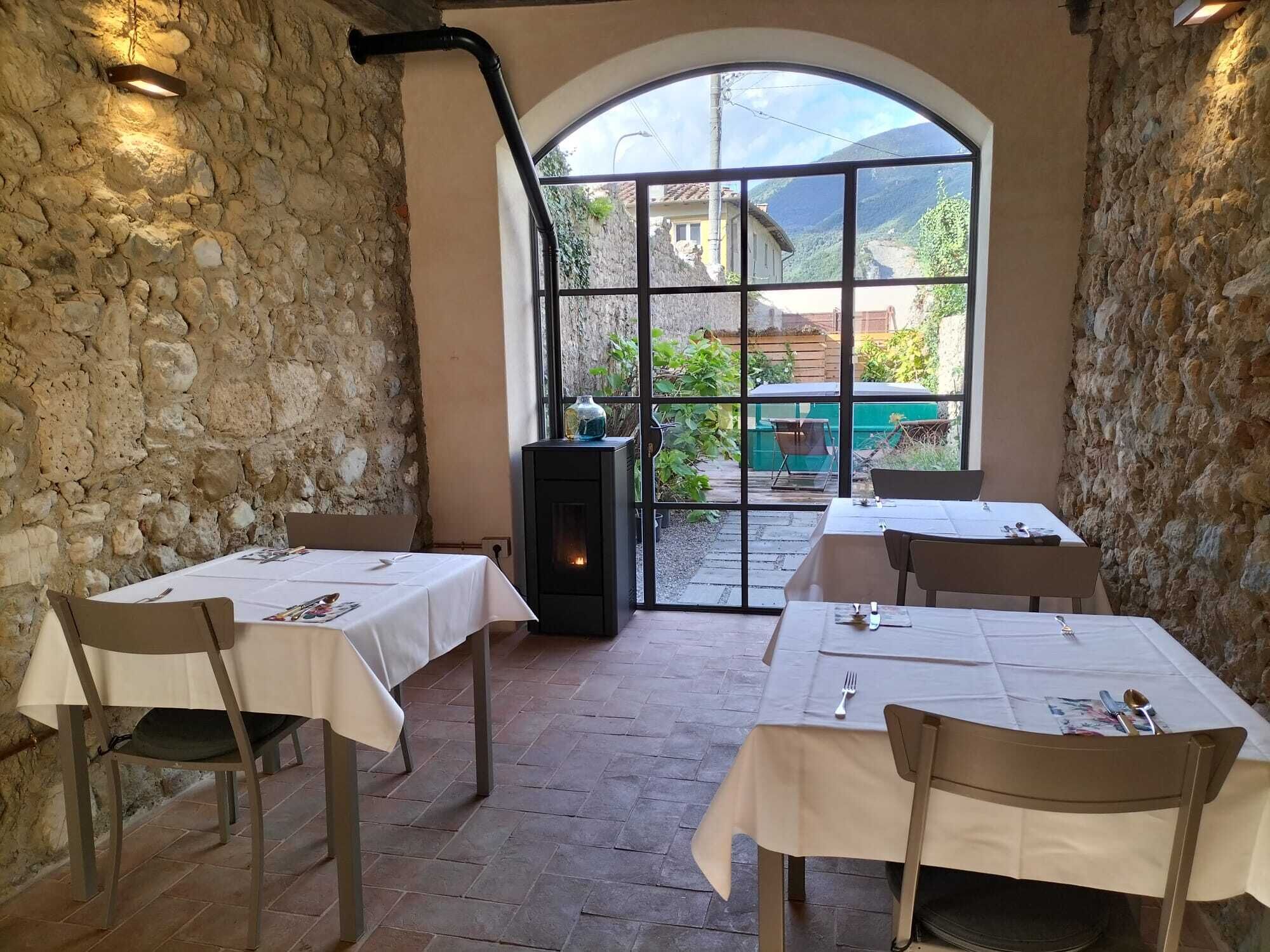 A restaurant with stone walls and a large arched window. Tables are set with white tablecloths and chairs.