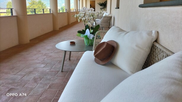 Un espace extérieur aménagé, abrité et doté d’un canapé, d’une petite table avec un saladier, et d’orchidées blanches.