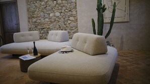 Un espace de détente moderne avec un mur en pierre, un grand cactus et un canapé agrémenté d’un chapeau et d’une bouteille de vin.