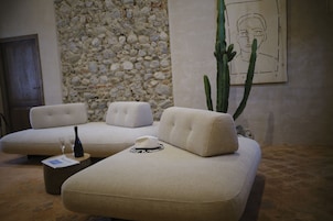 Un área lounge moderna con una pared de piedra, un cactus grande y un sofá con un sombrero y una botella de vino.