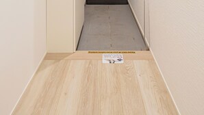 Un estrecho pasillo con suelo de madera, una puerta al final y un cuadro colgado en la pared.