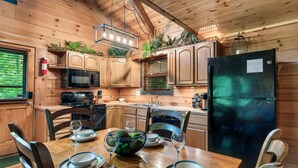 Cocina de cabaña de madera con una mesa de comedor lista para cuatro personas, un refrigerador y armarios de madera.