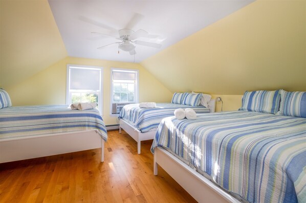 A room with two single beds, a ceiling fan, and large windows.