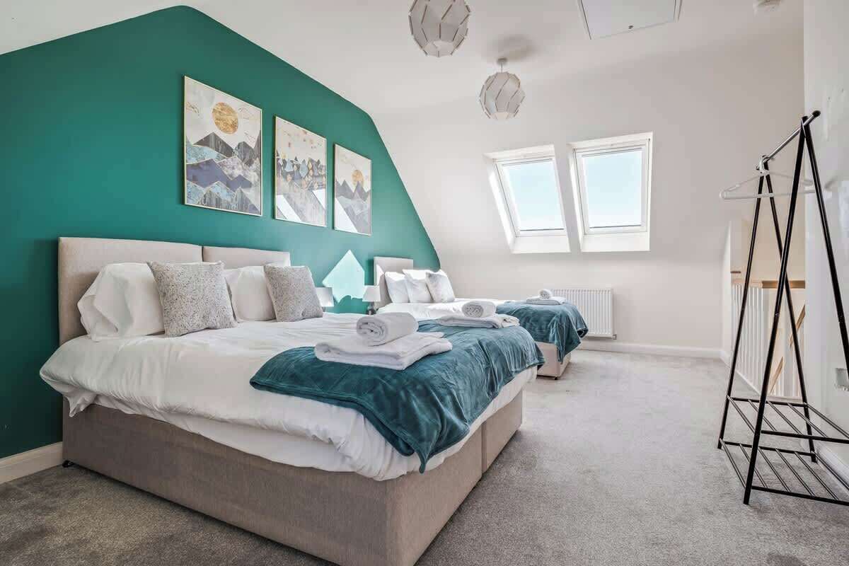 A bedroom with a large bed, two smaller beds, a window, and artwork on the wall.