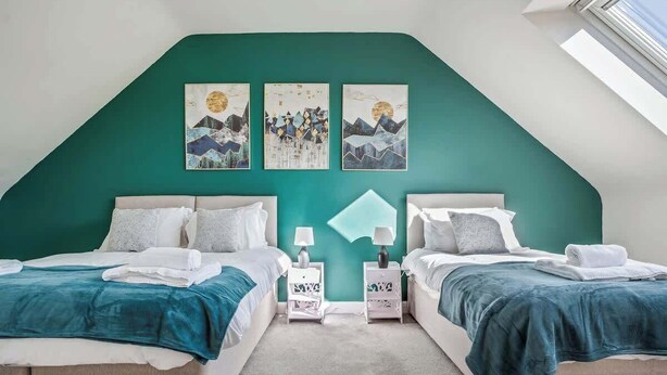 Een slaapkamer met twee bedden, teal muren en kunstwerken erboven.