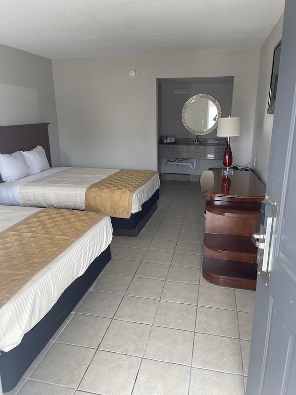 Habitación de hotel con dos camas, un tocador con espejo, una lámpara roja y un aparador de madera.
