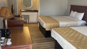 A hotel room with two single beds, a wooden desk with a lamp, a mirror, and a small vanity with a sink. - Branson Victorian Inn (Branson)