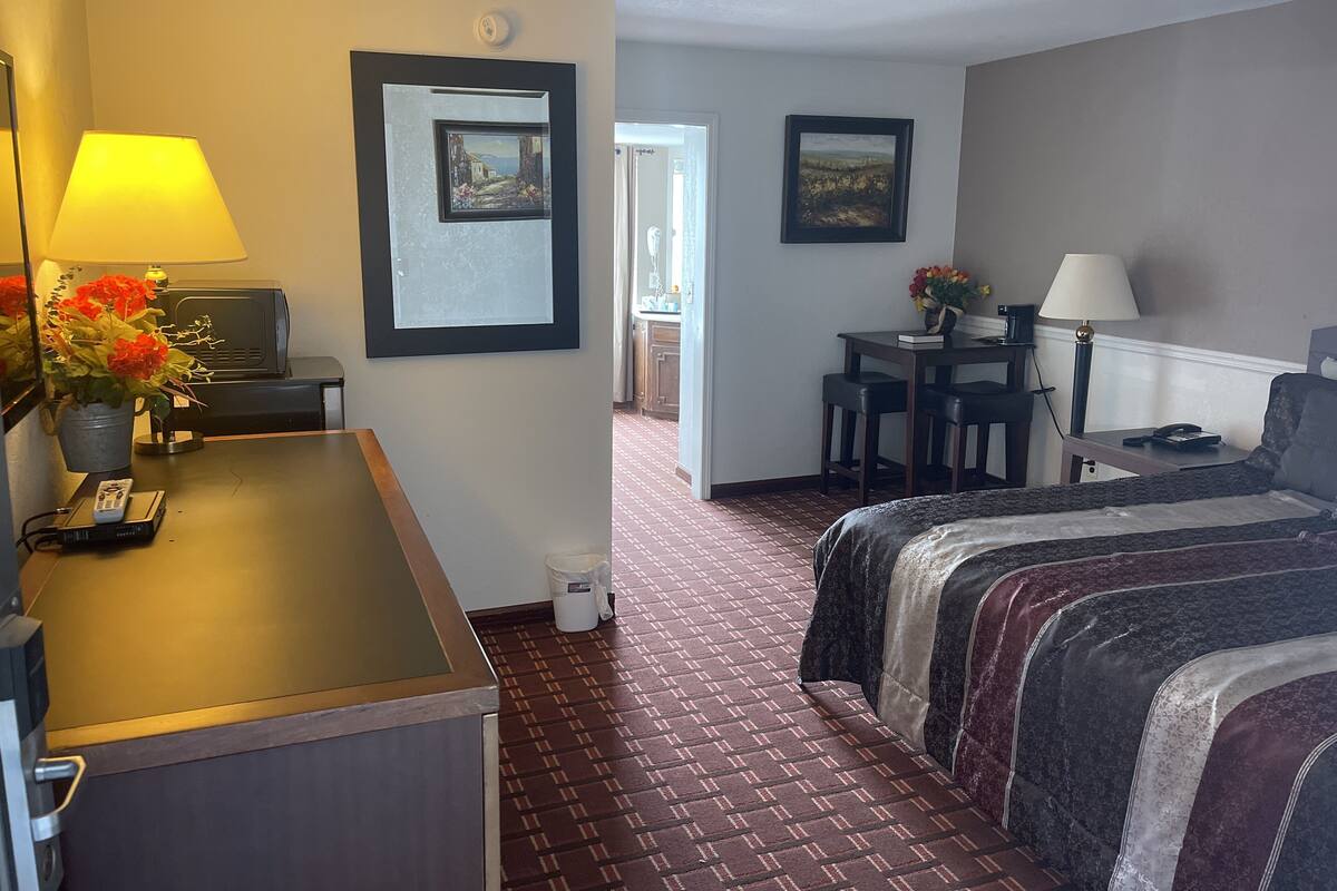 A hotel room with a bed, desk, chair, lamp, and a small table with a vase of flowers.
