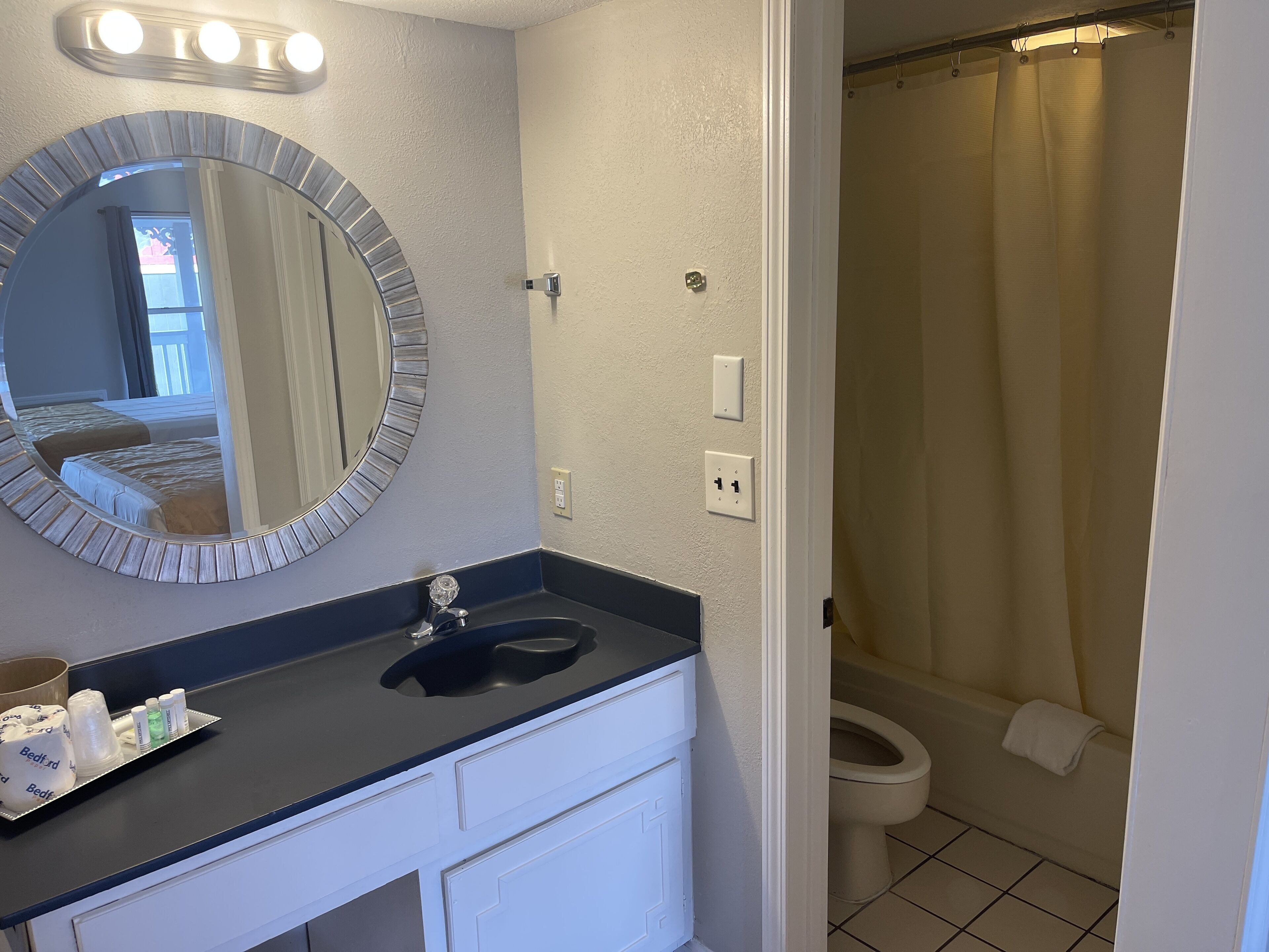 A bathroom with a sink, mirror, and toilet. There are toiletries on the counter and a shower curtain visible.