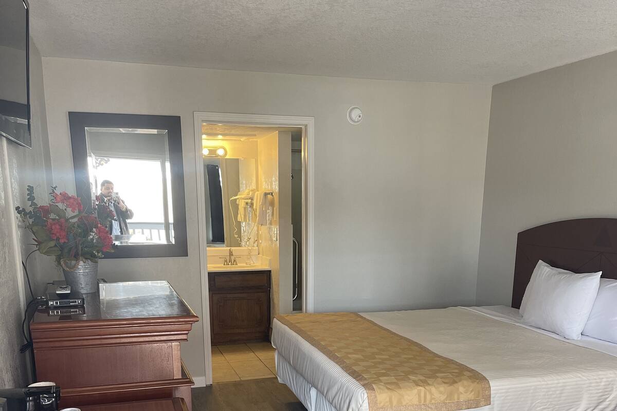 A hotel room with a bed, a desk with a coffee maker, a mirror, and a bathroom visible through an open door.