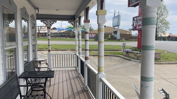A covered outdoor seating area with wooden flooring and metal benches. - Branson Victorian Inn (Branson)