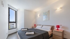 Une chambre à coucher comprenant un lit, deux tables de chevet, une fenêtre et une œuvre d’art accrochée au mur.