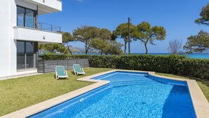 Une maison moderne à deux étages, dotée d’une piscine, de deux chaises longues et offrant une vue sur la mer.
